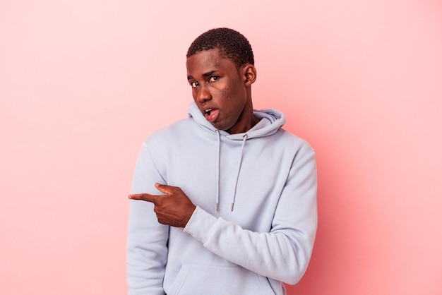 Jovem afro-americano isolado em fundo rosa sorrindo e apontando de lado mostrando algo no espaço em branco