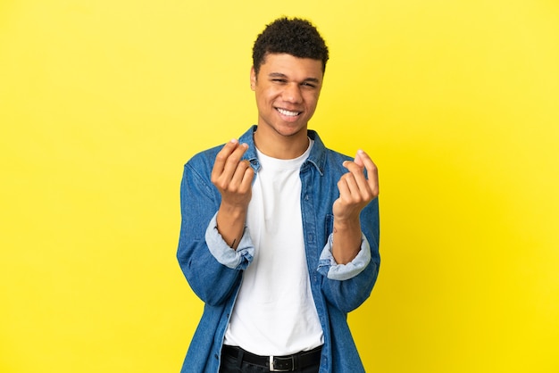 Jovem afro-americano isolado em um fundo amarelo fazendo gesto de dinheiro