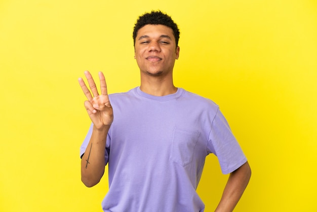 Jovem afro-americano isolado em um fundo amarelo feliz e contando três com os dedos