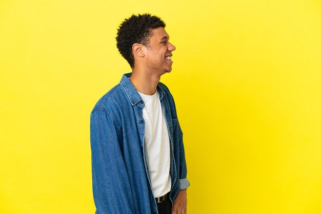 Jovem afro-americano isolado em um fundo amarelo rindo em posição lateral