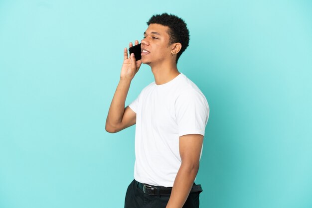 Jovem afro-americano isolado em um fundo azul, conversando com o celular