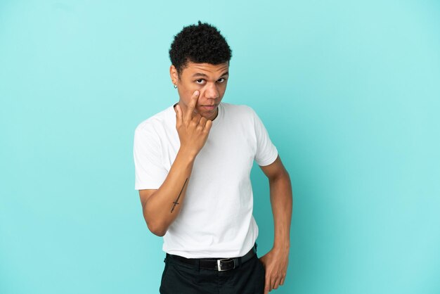 Jovem afro-americano isolado em um fundo azul mostrando algo