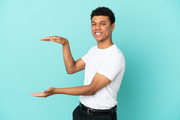 Jovem afro-americano isolado em um fundo azul segurando copyspace para inserir um anúncio