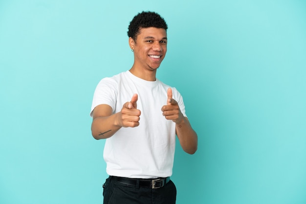 Jovem afro-americano isolado em um fundo azul surpreso e apontando para a frente