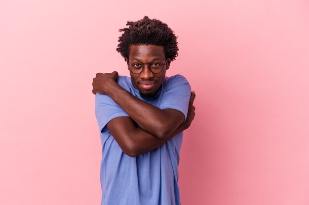 Jovem afro-americano isolado em um fundo rosa abraços, sorrindo despreocupado e feliz.