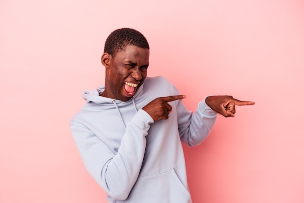 Jovem afro-americano isolado em um fundo rosa animado, apontando com os indicadores de distância.