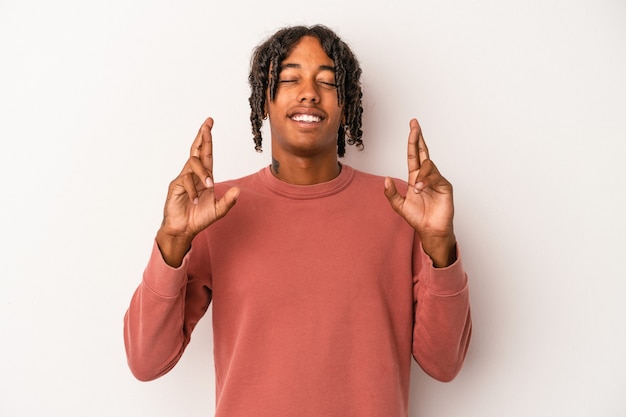 Jovem afro-americano isolado no fundo branco cruzando os dedos para ter sorte