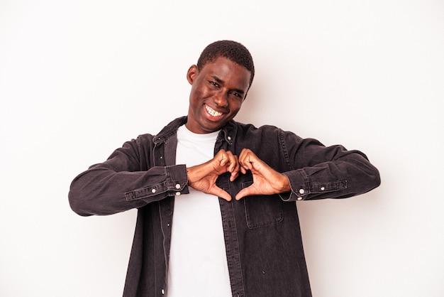 Jovem afro-americano isolado no fundo branco, sorrindo e mostrando uma forma de coração com as mãos.