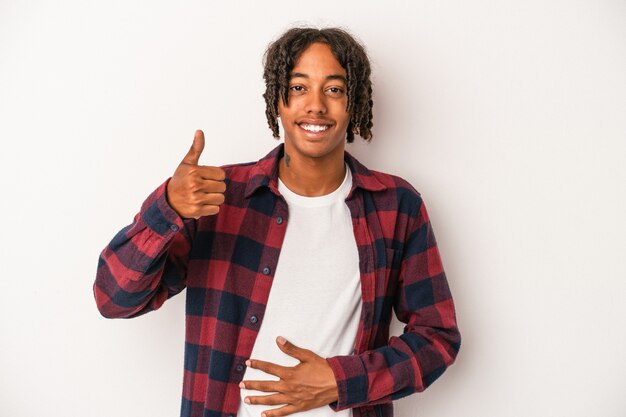 Jovem afro-americano isolado no fundo branco toca a barriga, sorri suavemente, comendo e o conceito de satisfação.