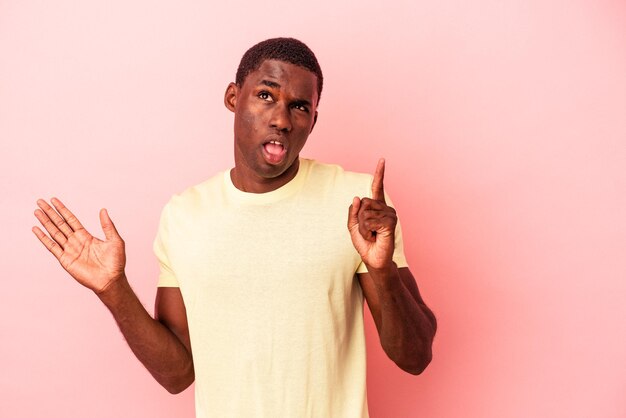 Jovem afro-americano isolado no fundo rosa segurando e mostrando um produto na mão.