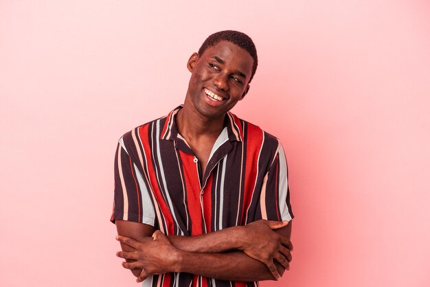 Jovem afro-americano isolado no fundo rosa sorrindo confiante com braços cruzados.