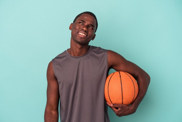 Jovem afro-americano jogando basquete isolado em um fundo azul, sonhando em alcançar objetivos e propósitos