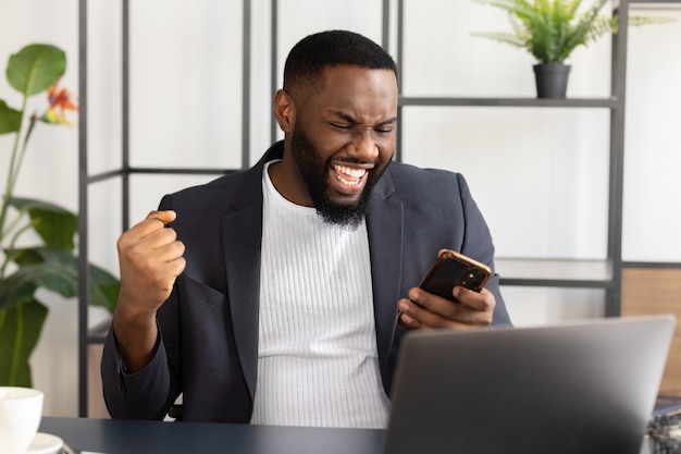 Jovem afro-americano lendo boas notícias inesperadas no smartphone