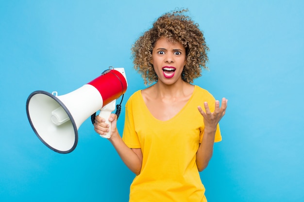 Jovem afro-americano olhando desesperado e frustrado, estressado, infeliz e irritado, gritando e gritando com um megafone