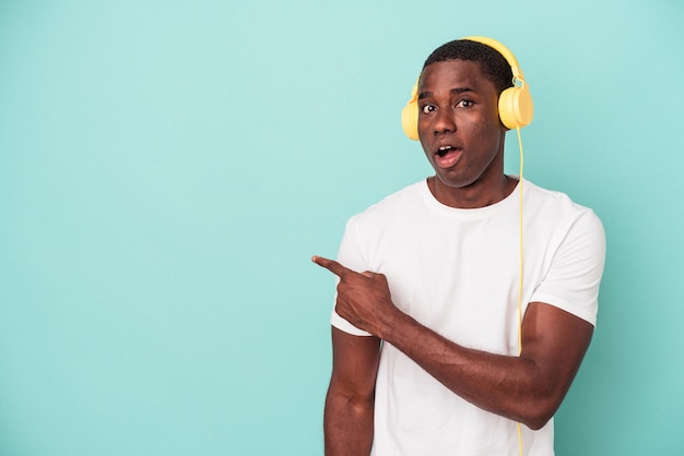 Jovem afro-americano ouvindo música isolada em fundo azul, apontando para o lado