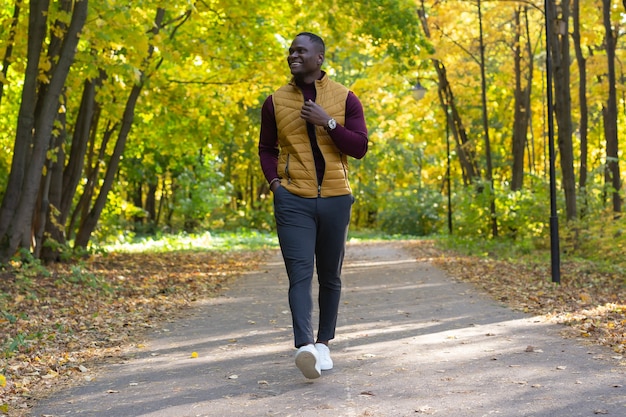 Foto jovem afro-americano positivo com roupas elegantes caminha pelo parque