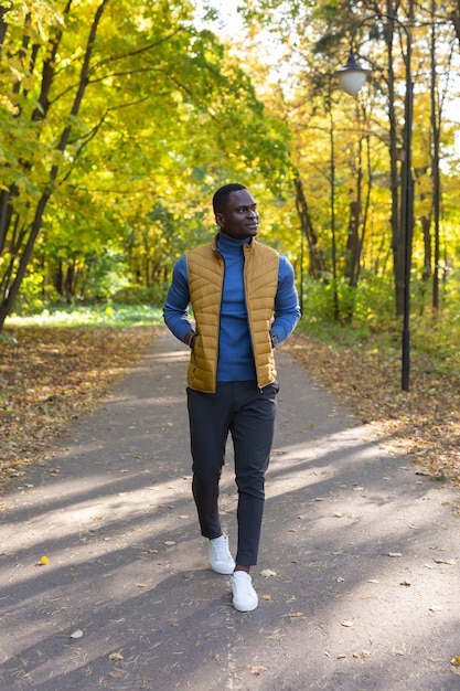 Foto jovem afro-americano positivo com roupas elegantes caminha pelo parque