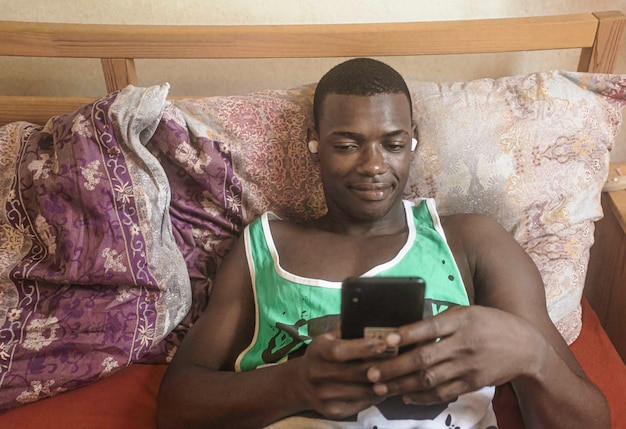 Jovem afro-americano relaxando na cama com música e celular