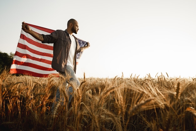 Jovem afro-americano segurando a bandeira nacional dos EUA no campo de trigo