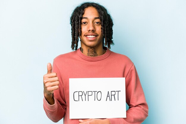 Jovem afro-americano segurando cartaz de arte criptográfica isolado em fundo azul sorrindo e levantando o polegar