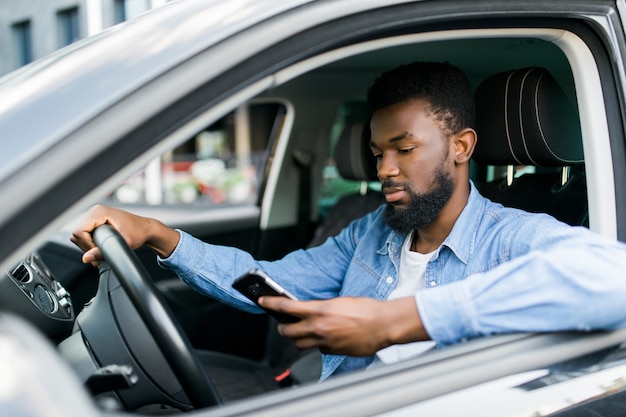 Foto jovem afro-americano segurando seu telefone enquanto dirige seu carro