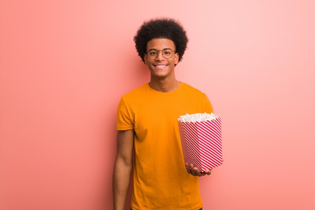 Jovem afro-americano segurando um balde de pipoca alegre com um grande sorriso