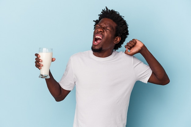 Jovem afro-americano segurando um copo de leite isolado em um fundo azul.