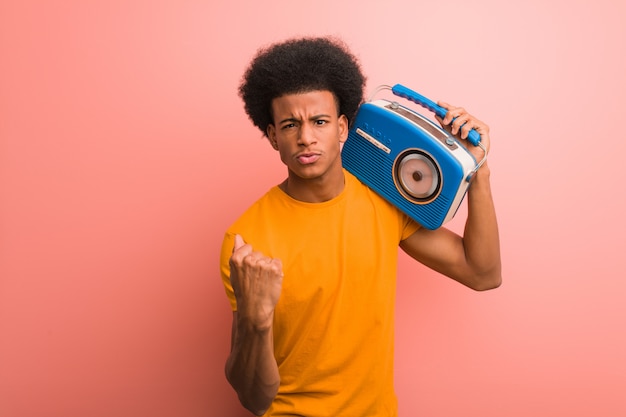 Jovem afro-americano segurando um rádio vintage, mostrando o punho para a frente, expressão de raiva