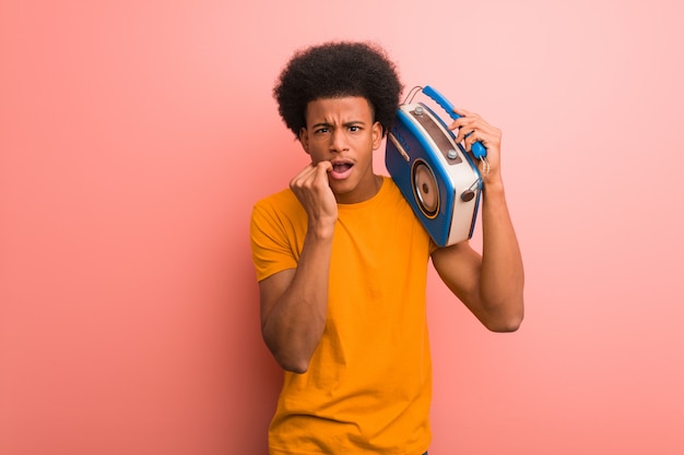 Jovem afro-americano segurando um rádio vintage roer unhas, nervoso e muito ansioso