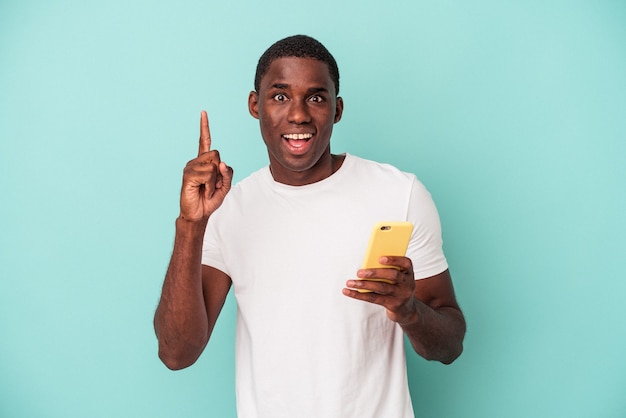 Jovem afro-americano segurando um telefone celular isolado em um fundo azul, tendo uma ótima ideia, o conceito de criatividade.