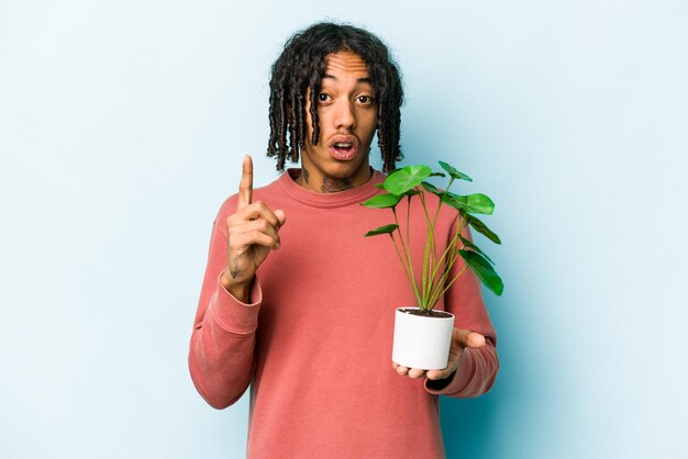 Jovem afro-americano segurando uma planta isolada em fundo azul com um conceito de inspiração de ideia