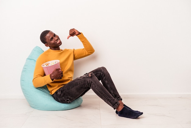Jovem afro-americano sentado em um sopro comendo pipoca isolada no fundo branco se sente orgulhoso e autoconfiante, exemplo a seguir.