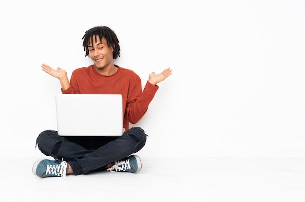 Jovem afro-americano sentado no chão e trabalhando com seu laptop segurando copyspace com as duas mãos