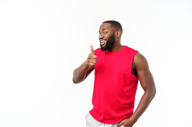 Jovem afro-americano sobre fundo isolado, vestindo roupas esportivas, sorrindo com uma cara feliz, olhando com o polegar para cima.