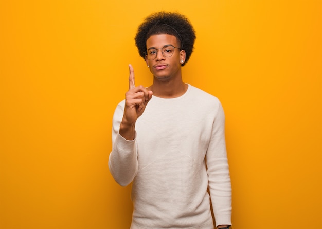 Jovem afro-americano sobre uma parede laranja, mostrando o número um