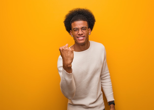 Jovem afro-americano sobre uma parede laranja, mostrando o punho