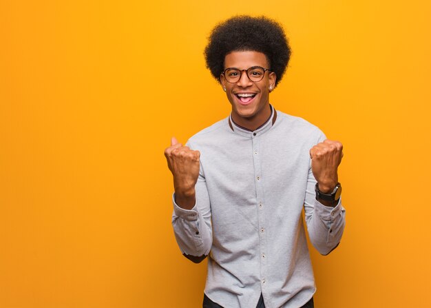 Jovem afro-americano sobre uma parede laranja surpreso e chocado