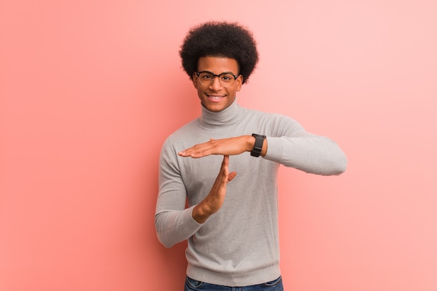 Jovem afro-americano sobre uma parede rosa, fazendo um gesto de tempo limite