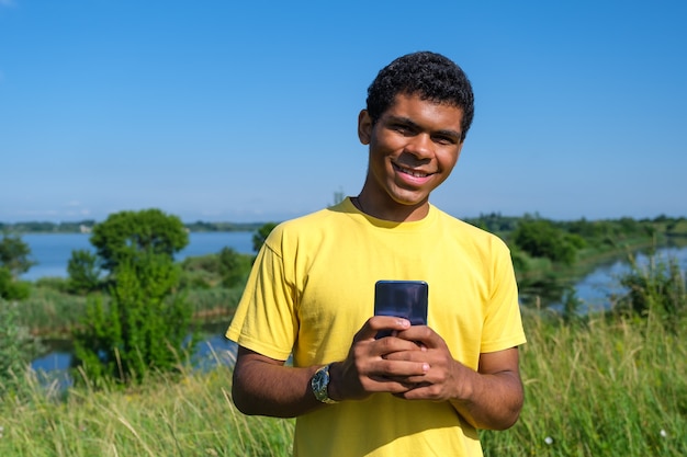 Jovem afro-americano sorridente se comunica em redes sociais ao ar livre