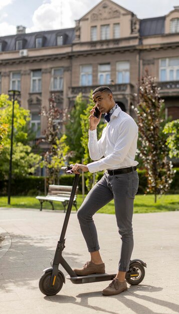 Jovem afro-americano usando telefone celular em pé com scooter elétrico em uma rua