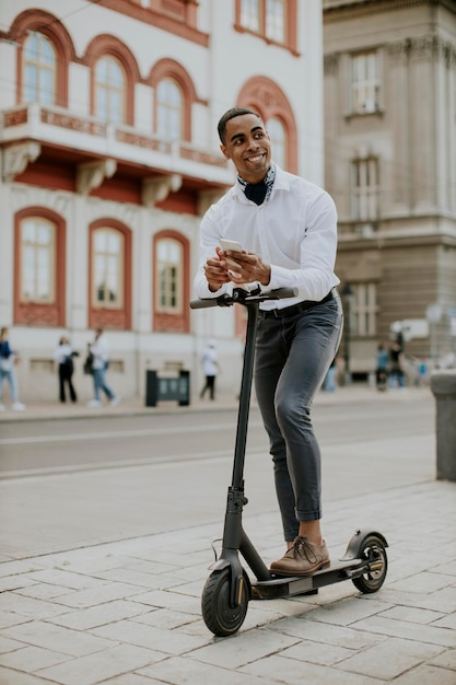 Jovem afro-americano usando telefone celular em pé com scooter elétrico em uma rua