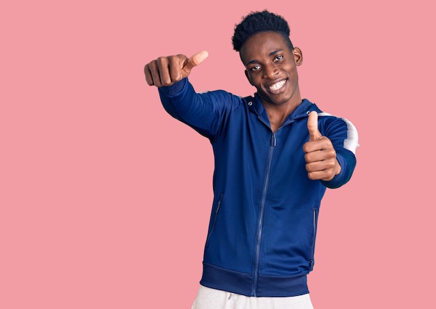 Jovem afro-americano vestindo roupas esportivas aprovando gesto positivo com a mão, polegares para cima sorrindo e feliz pelo sucesso. gesto vencedor.