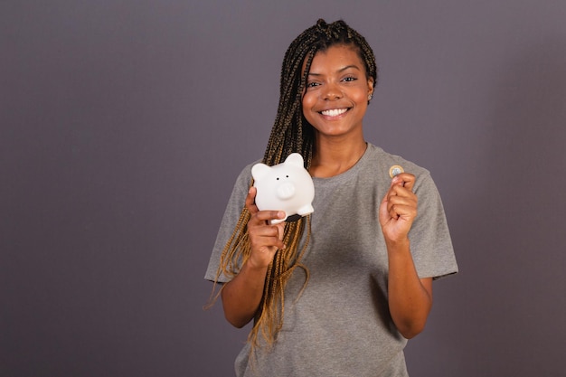 Jovem afro-brasileira segurando o cofrinho e o conceito de moeda de economia financeira