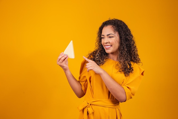 Jovem afro com uma fatia de queijo brie nas mãos apontando para ele