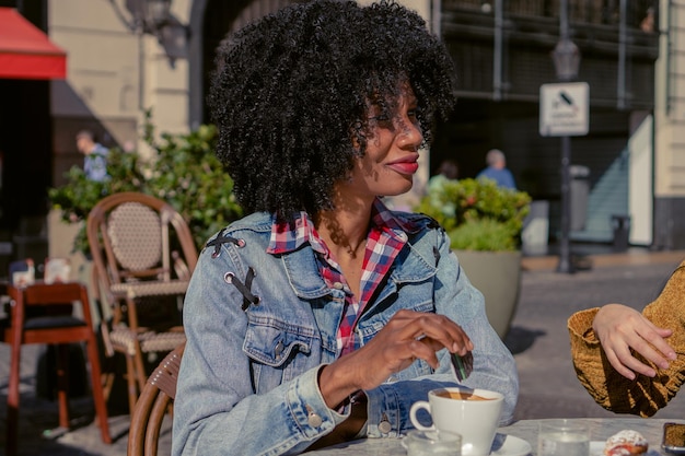 Jovem afro haitiana adoçando um café em um café ao ar livre no outono