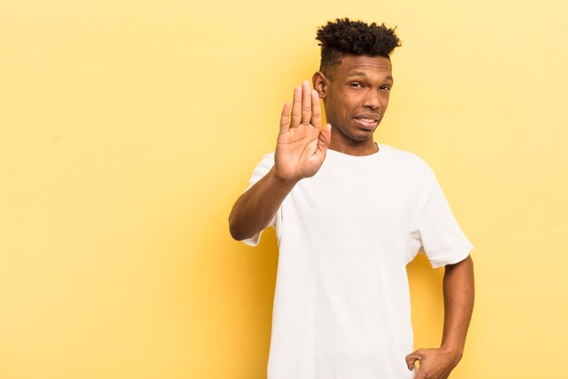 Jovem afro negro olhando sério mostrando a palma da mão aberta fazendo gesto de parada com um espaço de cópia ao lado