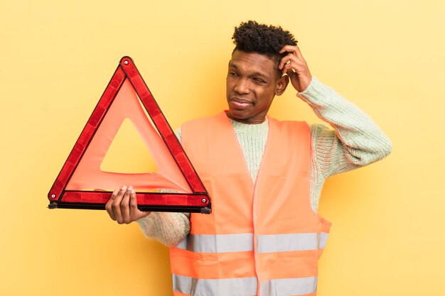 Jovem afro negro se sentindo confuso e confuso coçando a falha do carro e o conceito de triângulo