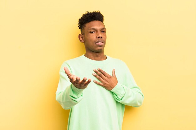 Jovem afro negro se sentindo feliz e apaixonado sorrindo com uma mão ao lado do coração e a outra esticada na frente