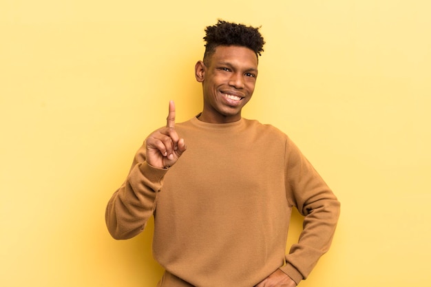Foto jovem afro negro sorrindo e parecendo amigável mostrando o número um ou primeiro com a mão em contagem regressiva