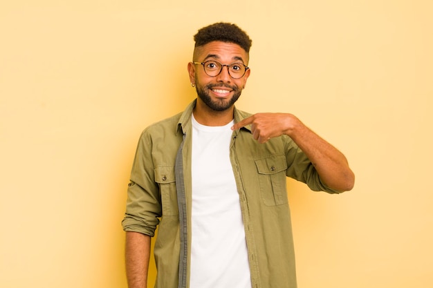 Jovem afro olhando feliz orgulhoso e surpreso apontando alegremente para se sentir confiante e elevado